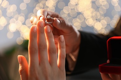 Photo of Making proposal. Man putting engagement ring on his girlfriend's finger indoors, closeup. Bokeh effect