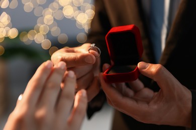 Photo of Man with engagement ring making marriage proposal to his girlfriend indoors, closeup. Bokeh effect