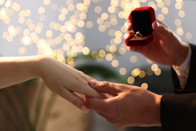 Photo of Man with engagement ring making marriage proposal to his girlfriend indoors, closeup. Bokeh effect