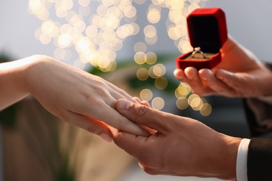 Photo of Man with engagement ring making marriage proposal to his girlfriend indoors, closeup. Bokeh effect