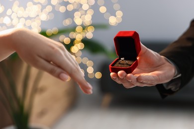 Photo of Man with engagement ring making marriage proposal to his girlfriend indoors, closeup. Bokeh effect