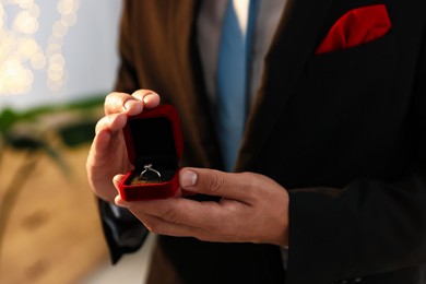 Photo of Making proposal. Man with engagement ring indoors, closeup. Bokeh effect