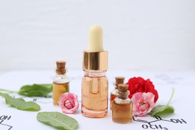 Photo of Bottles of cosmetic products, herbs and roses on paper with chemical formulas, closeup
