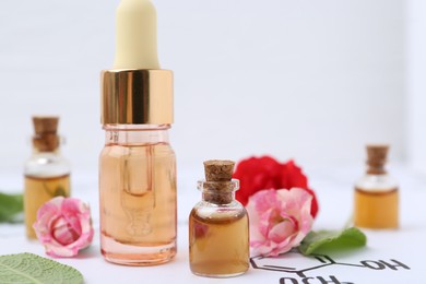 Photo of Bottles of cosmetic products, herbs and roses on paper with chemical formulas, closeup