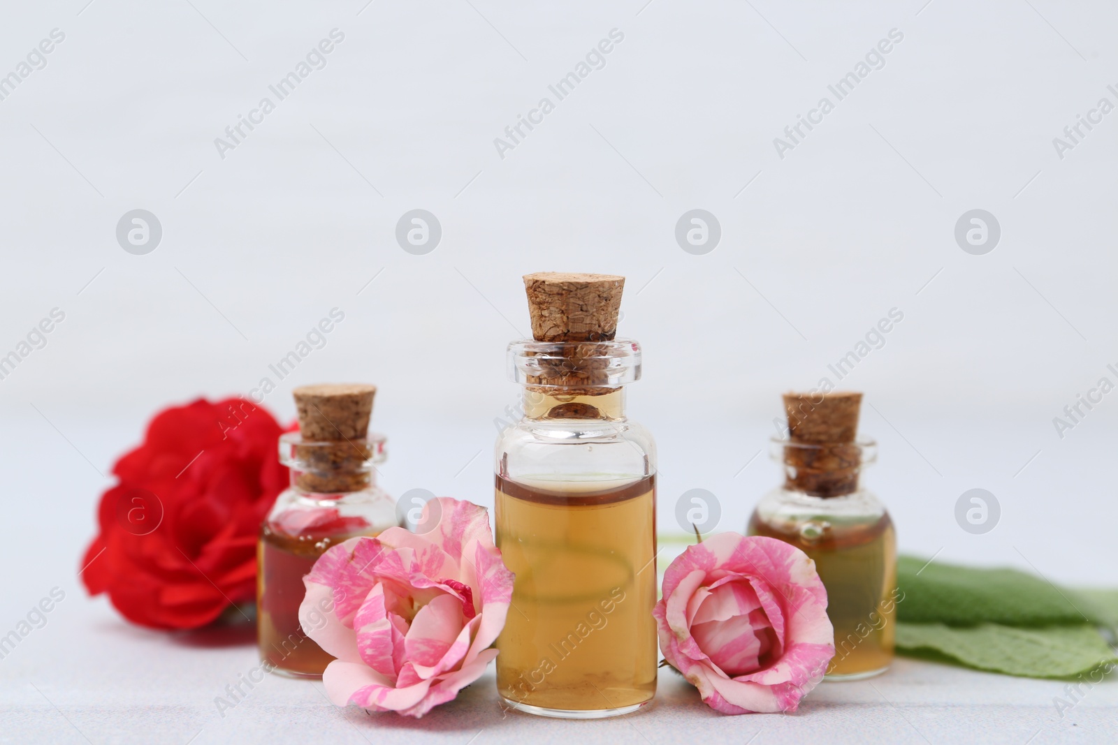 Photo of Bottles of cosmetic products, roses and sage on white table, closeup