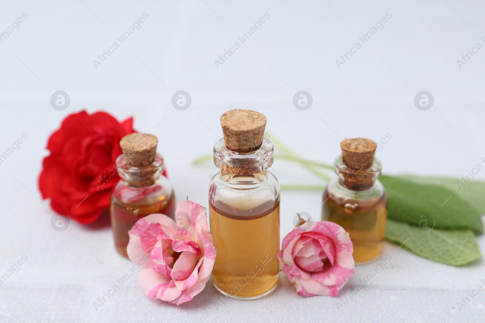 Photo of Bottles of cosmetic products, roses and sage on white table, closeup