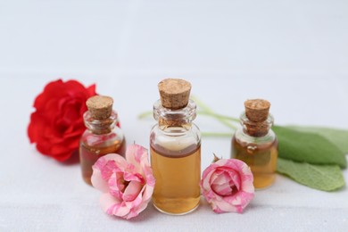 Photo of Bottles of cosmetic products, roses and sage on white table, closeup