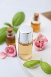 Photo of Bottles of cosmetic products, roses and basil on white table, closeup