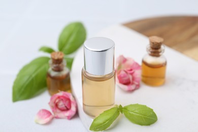 Photo of Bottles of cosmetic products, roses and basil on white table, closeup