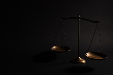 Photo of Golden scales of justice on black background, space for text