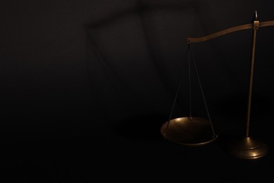 Photo of Golden scales of justice on black background, closeup. Space for text