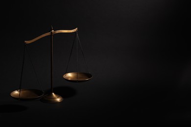 Photo of Golden scales of justice on black background, space for text
