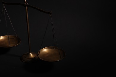 Photo of Golden scales of justice on black background, closeup. Space for text