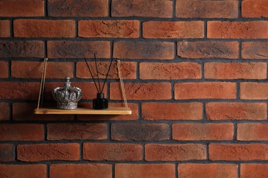 Photo of Wooden shelf with reed diffuser and home decor on brick wall, space for text
