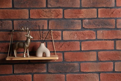 Photo of Wooden shelf with reed diffuser and home decor on brick wall, space for text