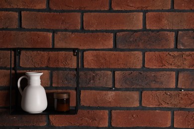 Photo of Square shaped shelf with vase and cosmetic product on brick wall, space for text