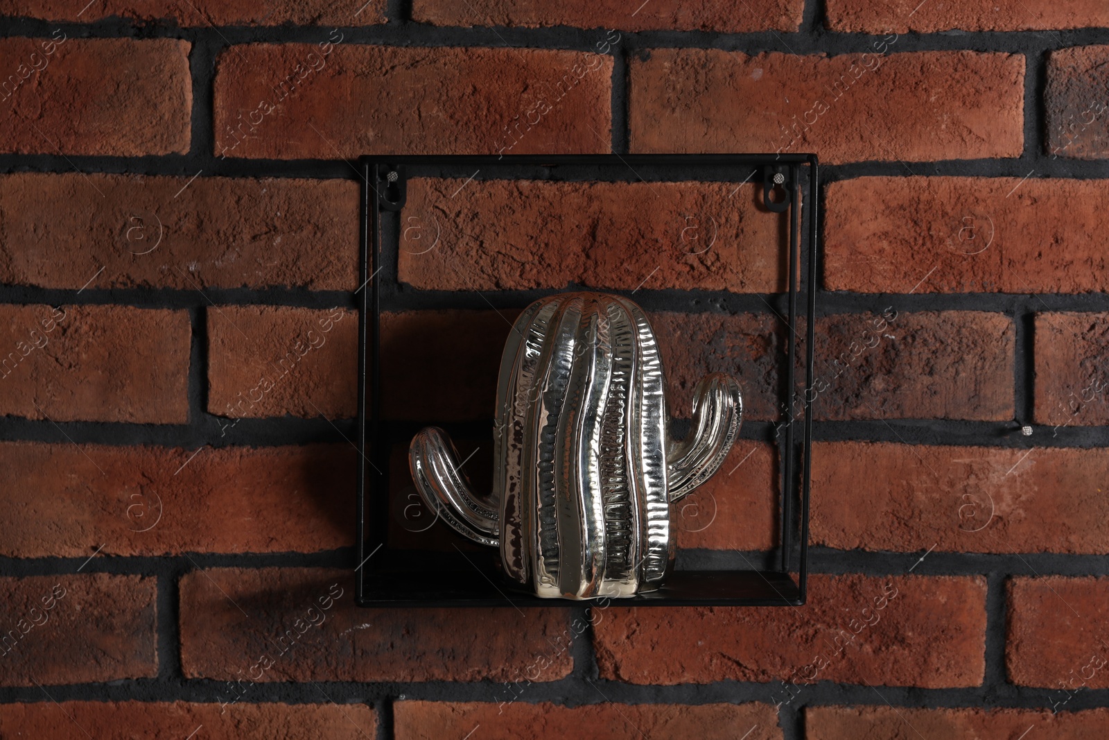 Photo of Square shaped shelf with cactus statue on brick wall