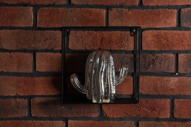 Photo of Square shaped shelf with cactus statue on brick wall