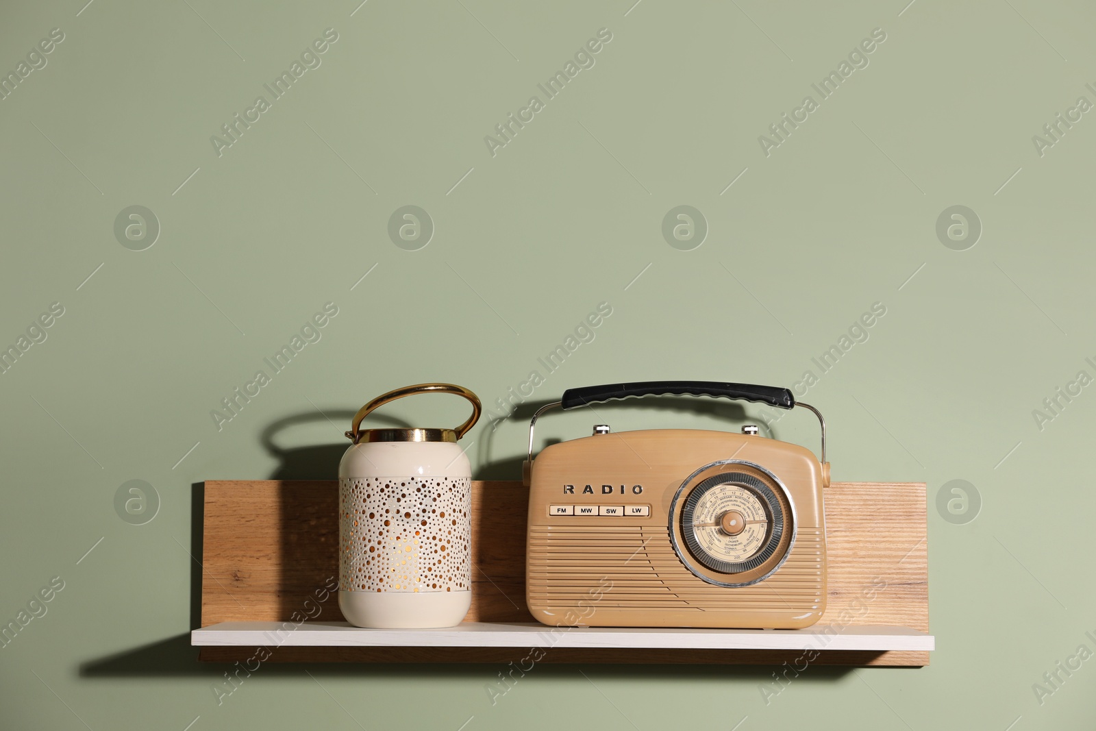 Photo of White wooden shelf with lamp and radio receiver on light green wall, space for text