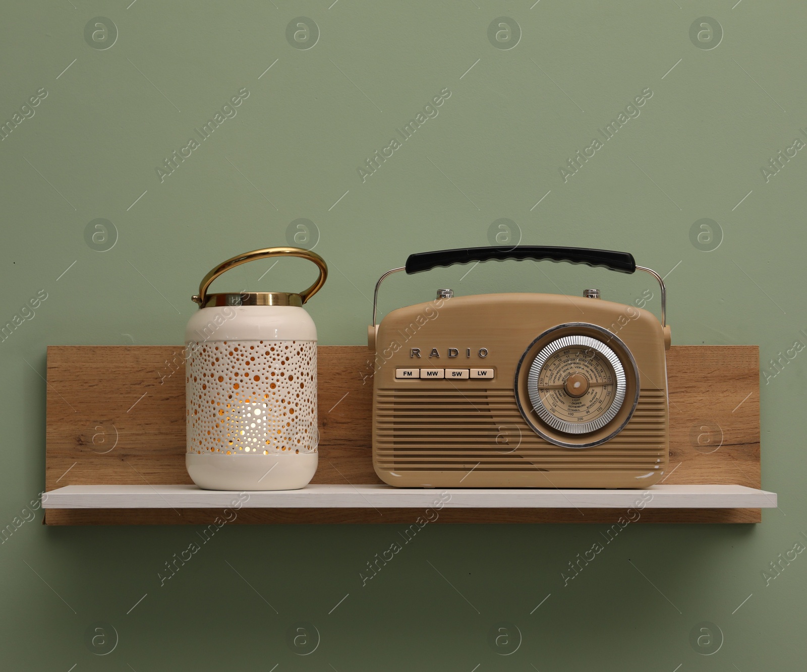 Photo of White wooden shelf with lamp and radio receiver on light green wall