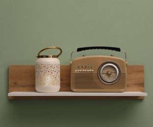 Photo of White wooden shelf with lamp and radio receiver on light green wall