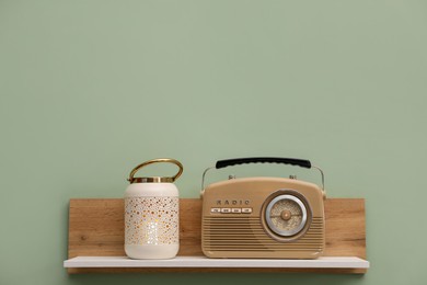 Photo of White wooden shelf with lamp and radio receiver on light green wall, space for text