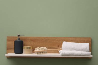 Photo of White wooden shelf with towels, brush and cosmetic products on light green wall, space for text