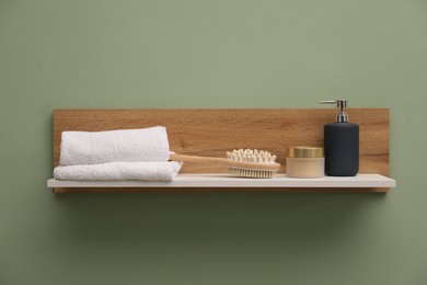 Photo of White wooden shelf with towels, brush and cosmetic products on light green wall