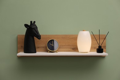 Photo of White wooden shelf with reed diffuser and home decor on light green wall
