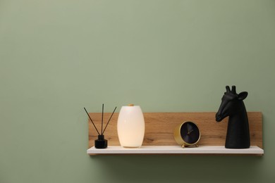 Photo of White wooden shelf with reed diffuser and home decor on light green wall, space for text