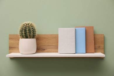 Photo of White wooden shelf with books and cactus on light green wall