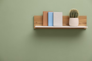 Photo of White wooden shelf with books and cactus on light green wall