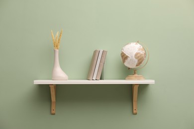 Photo of White shelf with books and home decor on light green wall