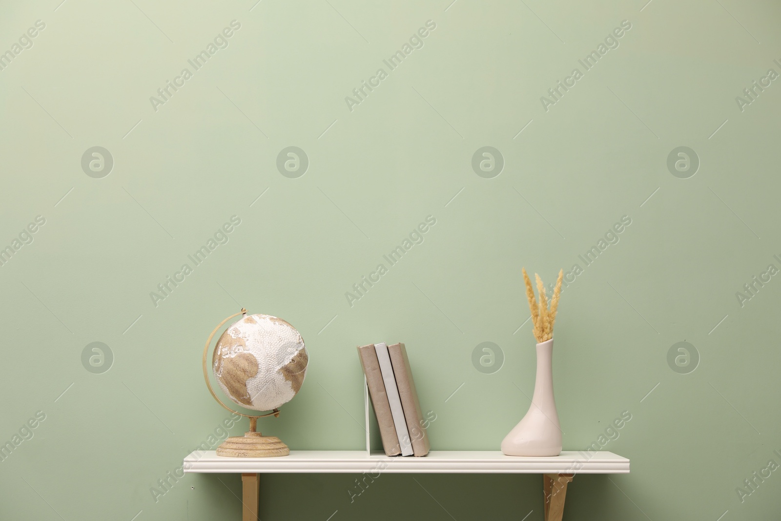 Photo of White shelf with books and home decor on light green wall, space for text