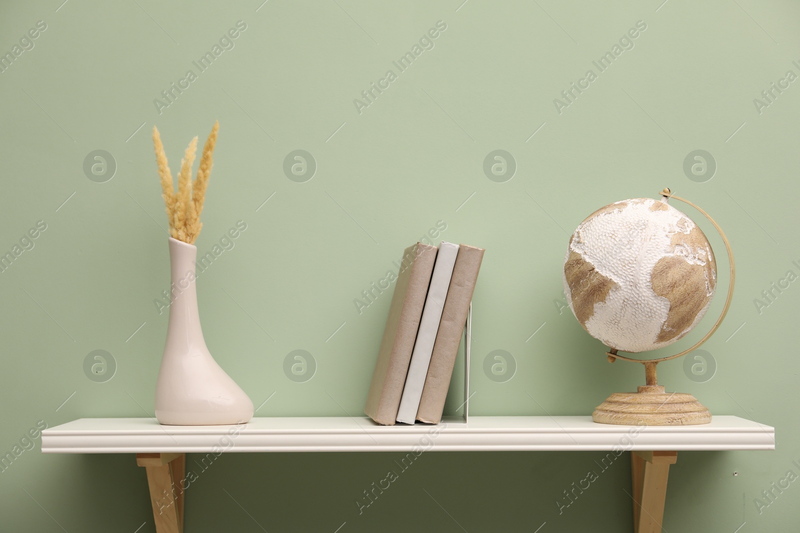 Photo of White shelf with books and home decor on light green wall