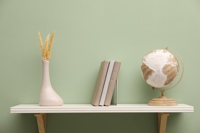 Photo of White shelf with books and home decor on light green wall