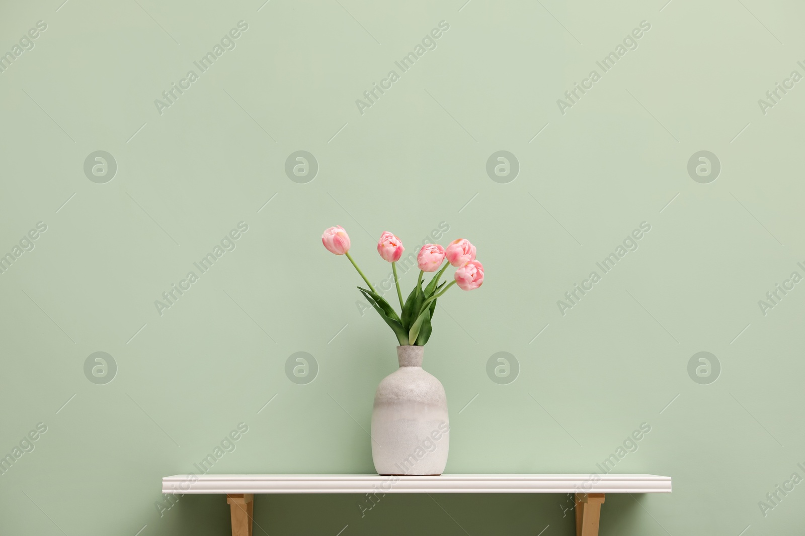 Photo of White shelf with vase of pink tulips on light green wall, space for text