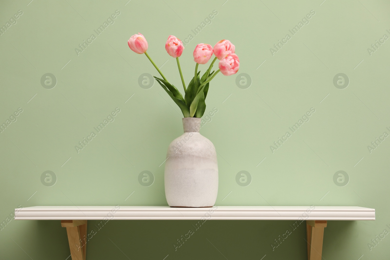 Photo of White shelf with vase of pink tulips on light green wall