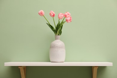 Photo of White shelf with vase of pink tulips on light green wall