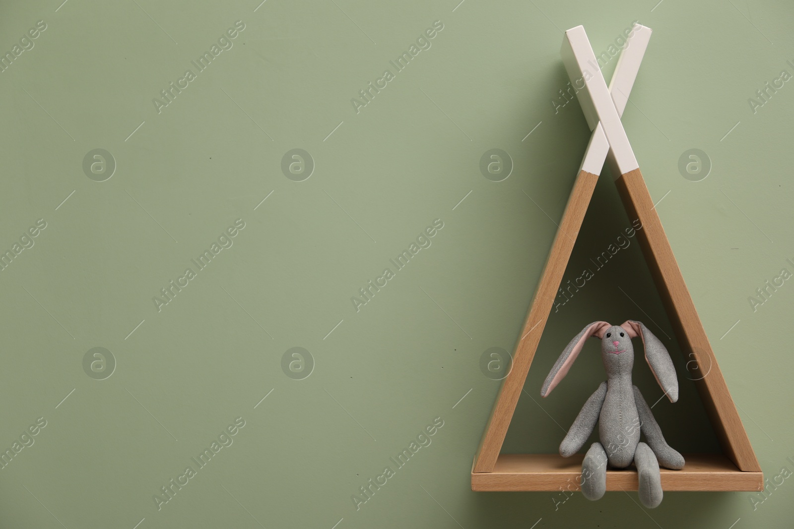 Photo of Triangle shaped shelf with bunny toy on light green wall, space for text