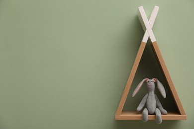 Photo of Triangle shaped shelf with bunny toy on light green wall, space for text