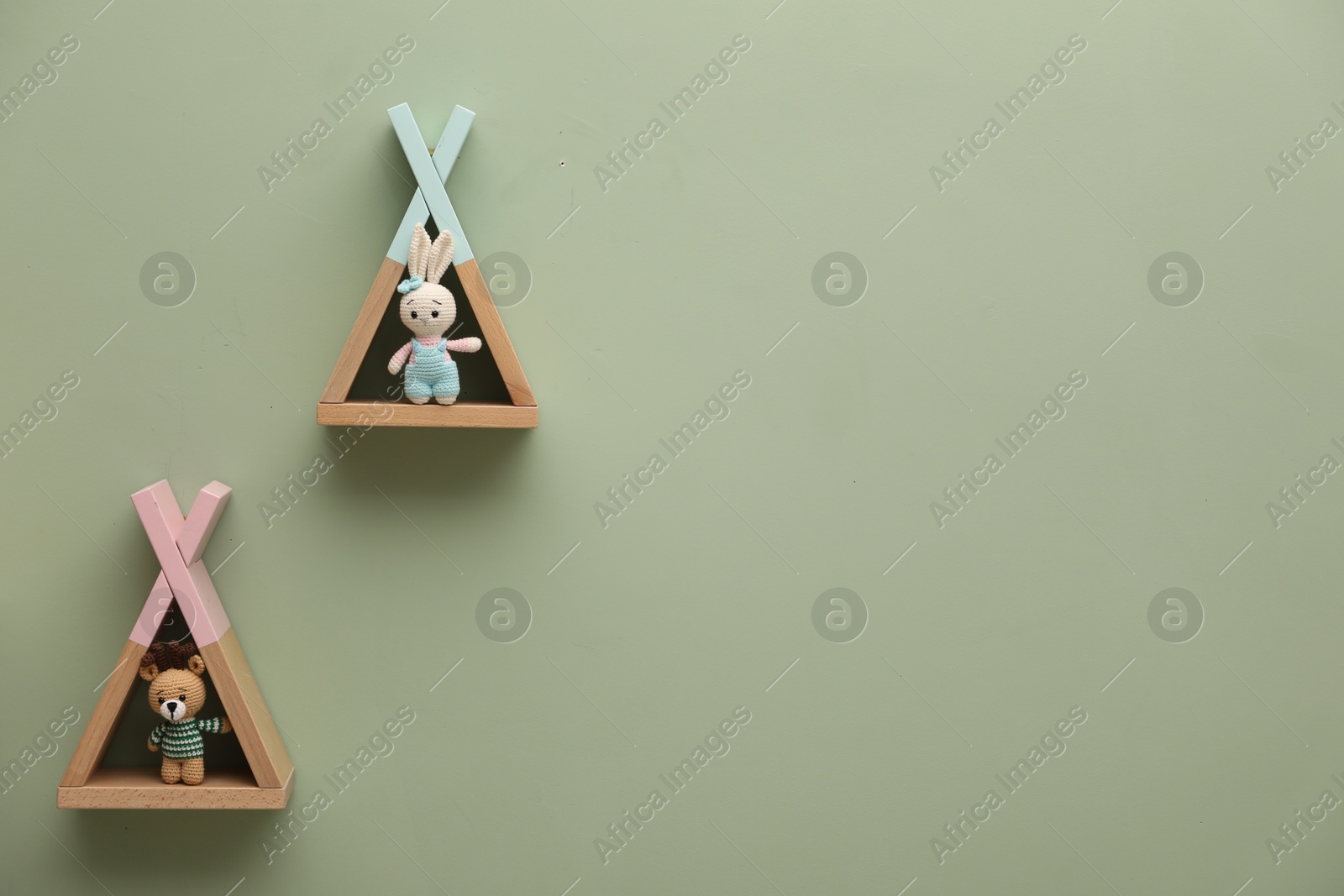 Photo of Triangle shaped shelves with toys on light green wall, space for text