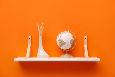 Photo of White shelf with vase and globe on orange wall