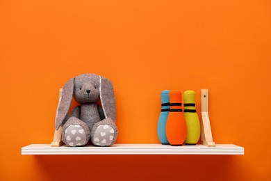 Photo of White shelf with toy bunny and bowling pins on orange wall, space for text