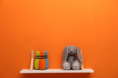 Photo of White shelf with toy bunny and bowling pins on orange wall, space for text