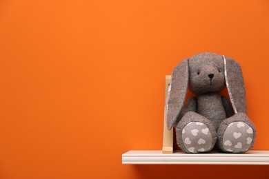Photo of White shelf with toy bunny on orange wall, space for text