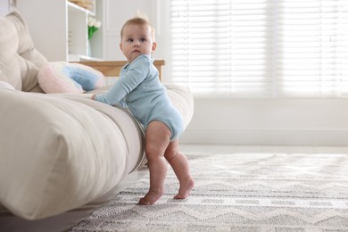 Photo of Cute little baby near sofa at home, space for text