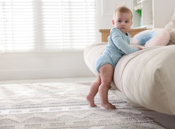 Photo of Cute little baby near sofa at home, space for text