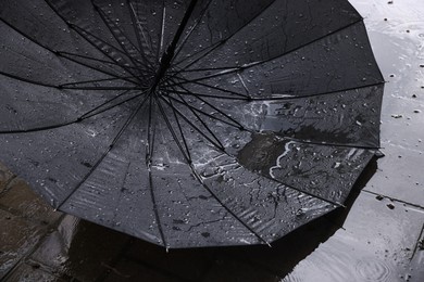 Photo of Black umbrella on wet asphalt under heavy rain, closeup