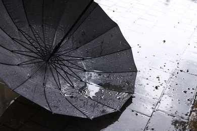 Photo of Black umbrella on wet asphalt under heavy rain, closeup. Space for text
